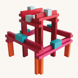 Brightly coloured Naef Tigno precision wooden stacking toy showing geometric construction in red, orange, blue, and pink blocks. Premium German made wooden puzzle and design object.