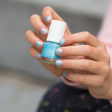 A closeup of a child's hand holding the Namaki kids' non-toxic nail polish, with the frosted blue nail polish on their nails.