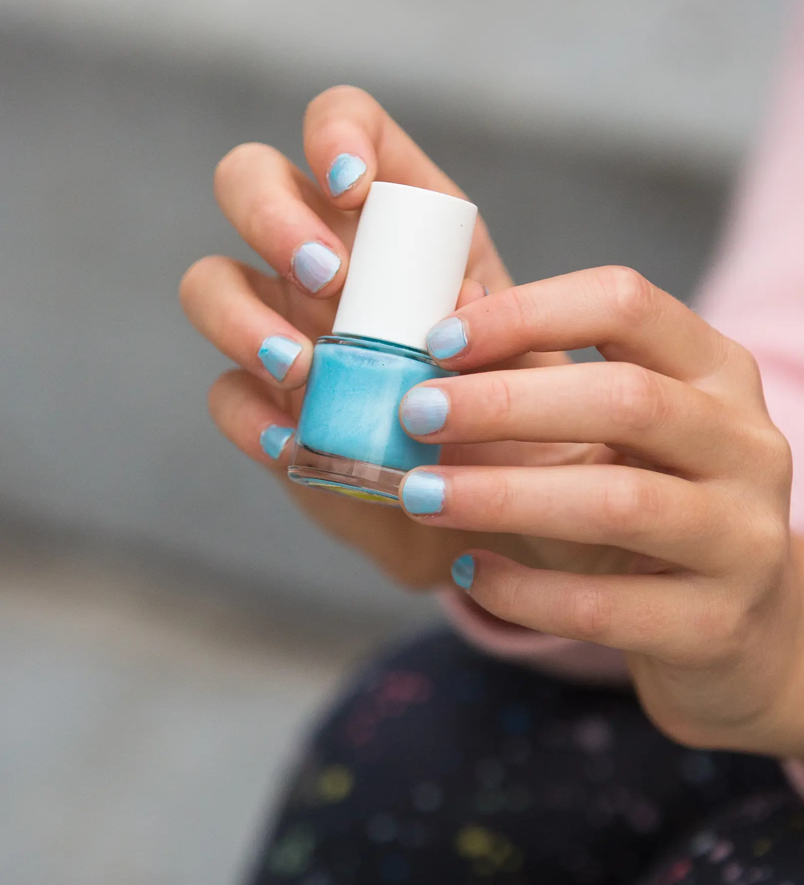 A closeup of a child's hand holding the Namaki kids' non-toxic nail polish, with the frosted blue nail polish on their nails.