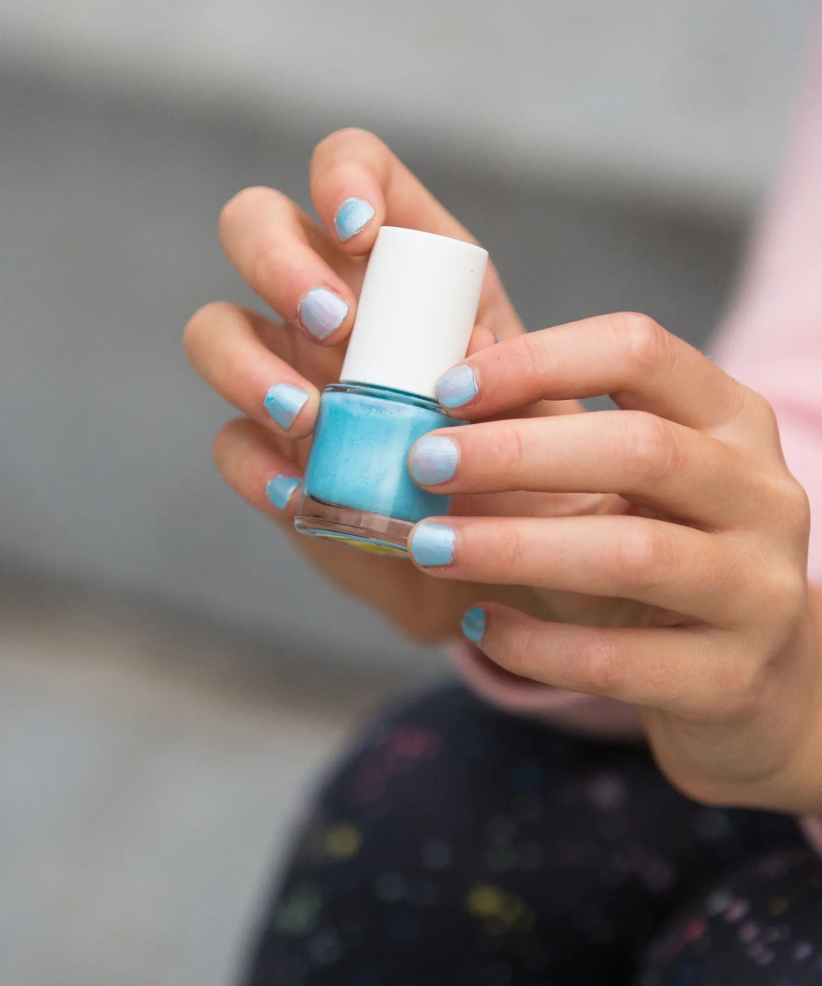 A closeup of a child's hand holding the Namaki kids' non-toxic nail polish, with the frosted blue nail polish on their nails.