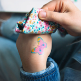 A closeup of a child's hand, applying a Namaki non-toxic temporary butterfly tattoo.
