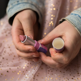 A closeup of a child's hands holding the Namaki natural kids' raspberry lip balm from the Nightingale makeup giftset