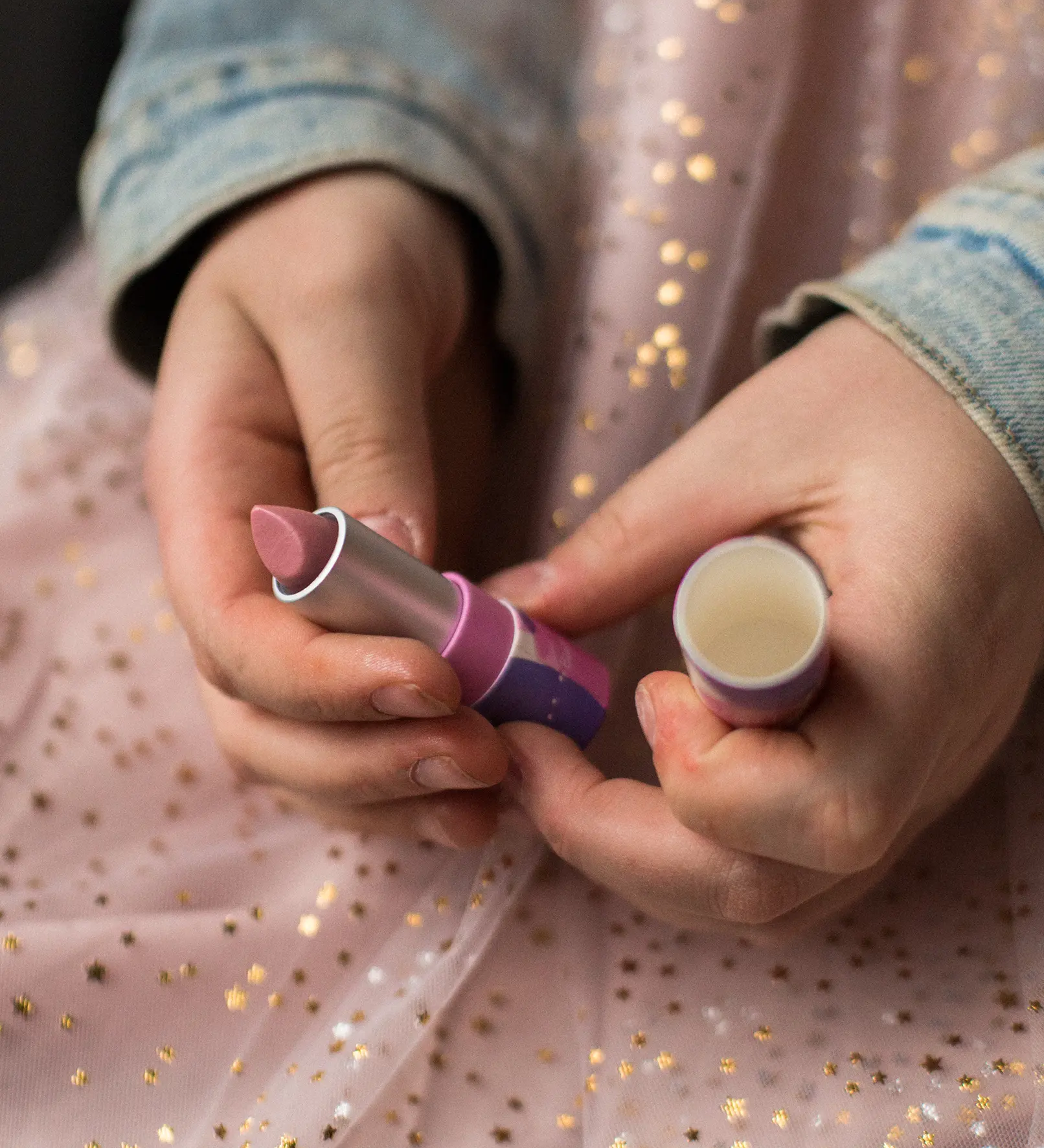 A closeup of a child's hands holding the Namaki natural kids' raspberry lip balm from the Nightingale makeup giftset