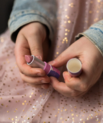 A closeup of a child's hands holding the Namaki natural kids' raspberry lip balm from the Nightingale makeup giftset