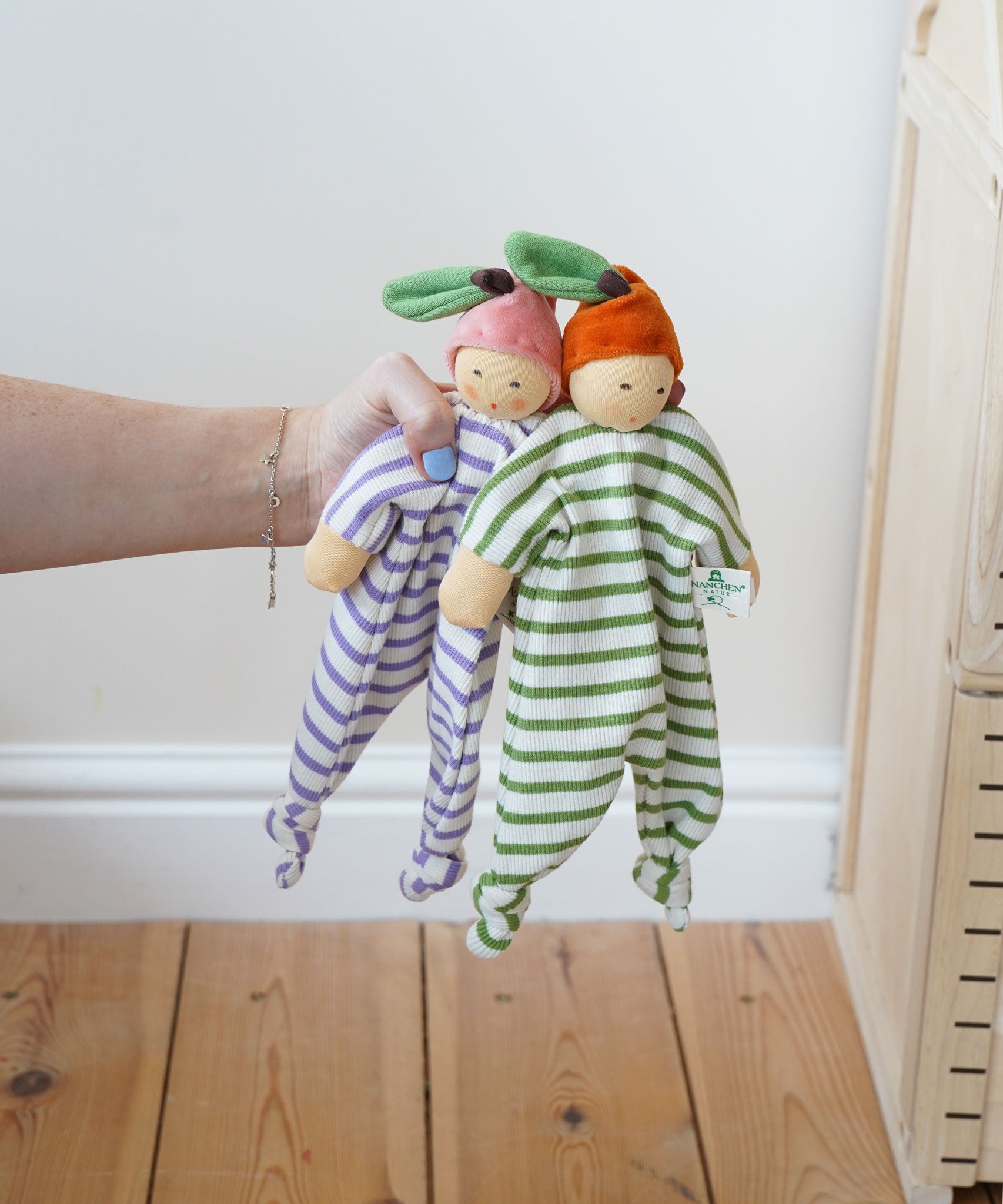 Nanchen peach and orange Baby Comforter Dolls being held up in an adult's hand.