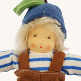 Close-up of the face of the Nanchen organic Waldorf doll Bela Blueberry. The doll has pale skin, hand-painted facial features, rosy cheeks, and wears a blue fruit-style hat with a green leaf and stem over messy blond hair.