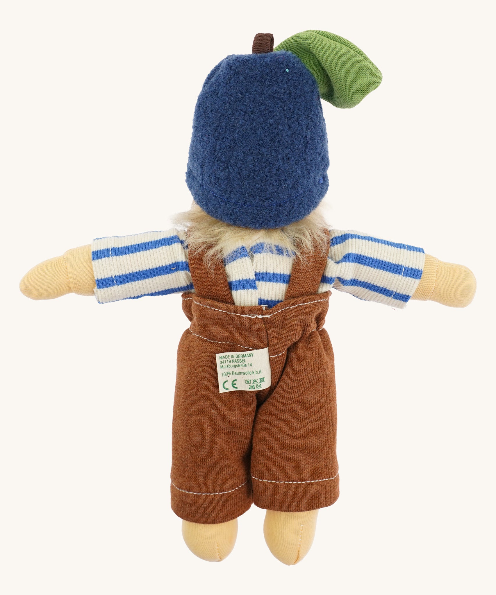 Back view of the Nanchen organic Waldorf doll named Bela Blueberry, dressed in a blue and white striped top, brown dungarees, and a soft blue fruit-style hat with a green leaf and brown stem. The doll has pale skin and fluffy blond hair peeking out from the hat.