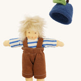 Nanchen organic Waldorf doll dressed in the blue and white striped top and brown dungarees, with the blueberry fruit hat beside it. The doll has pale skin and fluffy platinum blond hair.