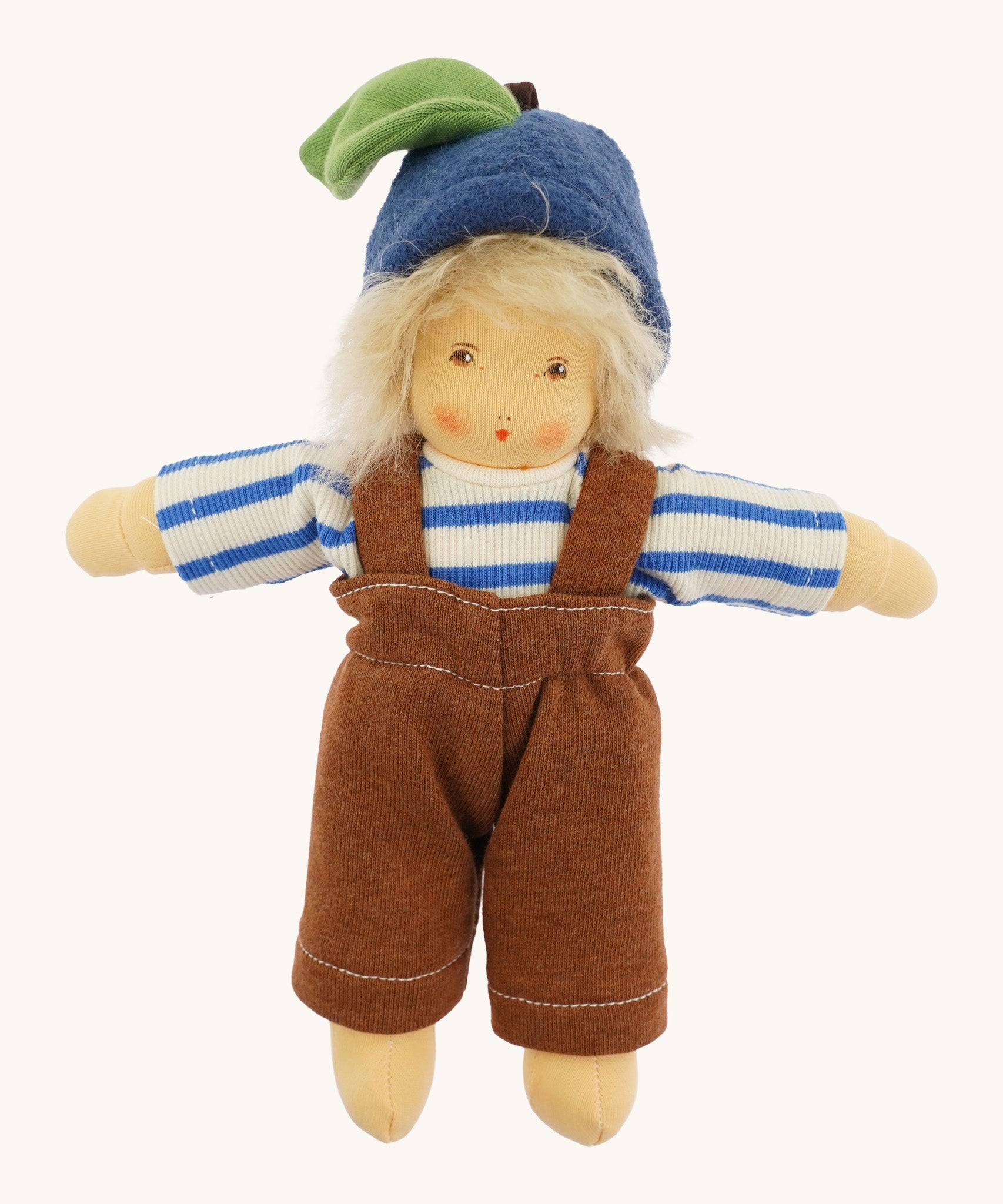 Front view of the Nanchen organic Waldorf doll Bela Blueberry, fully dressed in a blue and white striped long-sleeve top, brown dungarees, and a blue woollen fruit-style hat with a green leaf detail. The doll has soft blond hair and a gentle hand-painted expression.