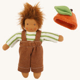Nanchen organic Waldorf doll dressed in a green and white striped top and brown dungarees, with the orange fruit hat placed beside it. The doll has brown skin and fluffy brown hair.