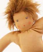 Close-up of a Nanchen organic Waldorf doll with brown skin and wild, fluffy brown hair. The doll has hand-painted eyes and a red dot mouth with blushed cheeks.