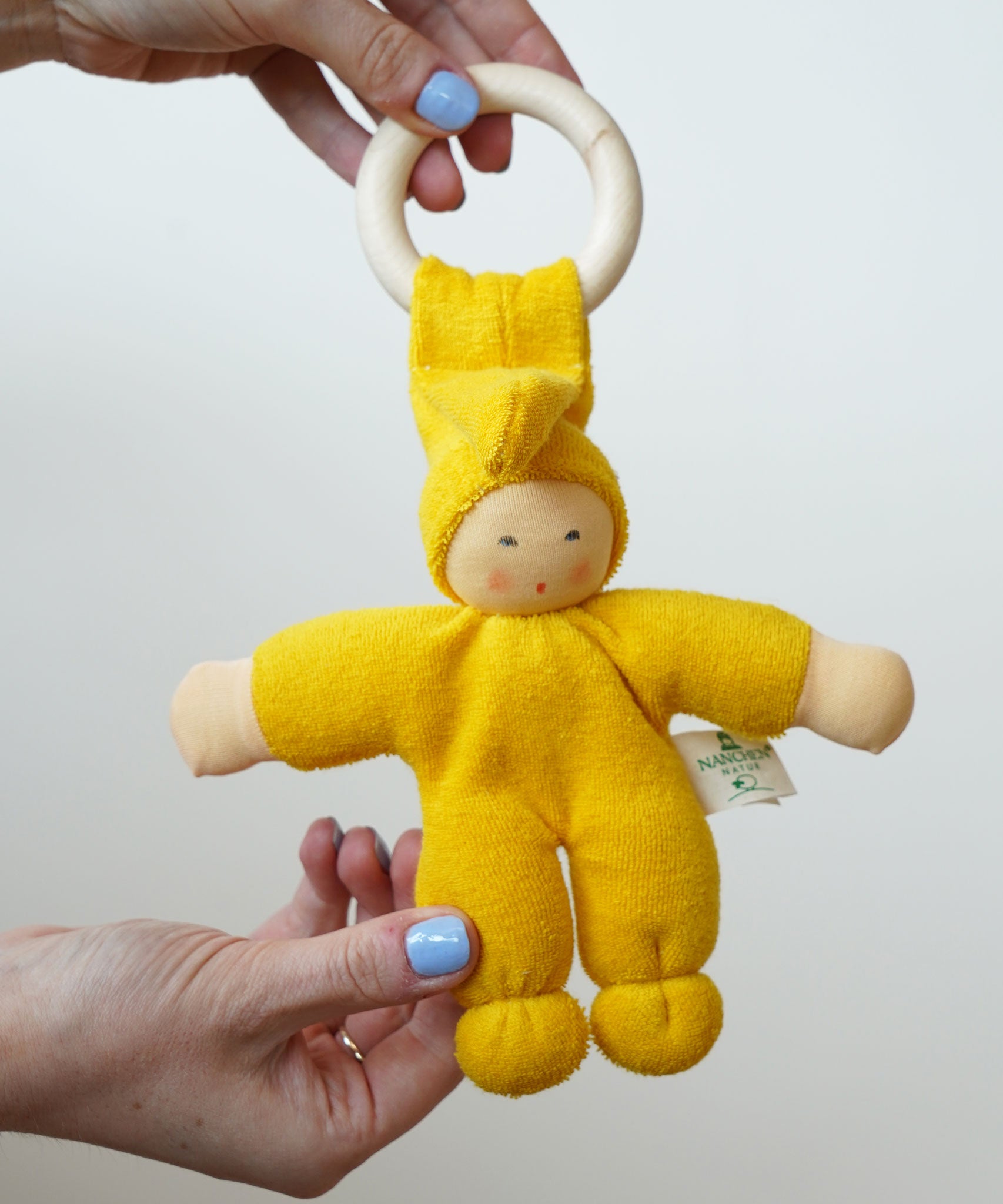 A close up of a yellow Nanchen pimpel doll in an adult's hand.
