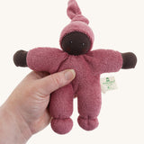 A Nanchen Pimpel Waldorf Handcrafted Doll with a berry pink coloured outfit an matching knotted hat in an adult's hand.
