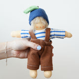 A Organic Handcrafted Nanchen Blueberry Child Waldorf Doll called Bella. The doll has a removable outfit which consists of a blue and white striped top, brown dungaree style bottoms and a blueberry hat.