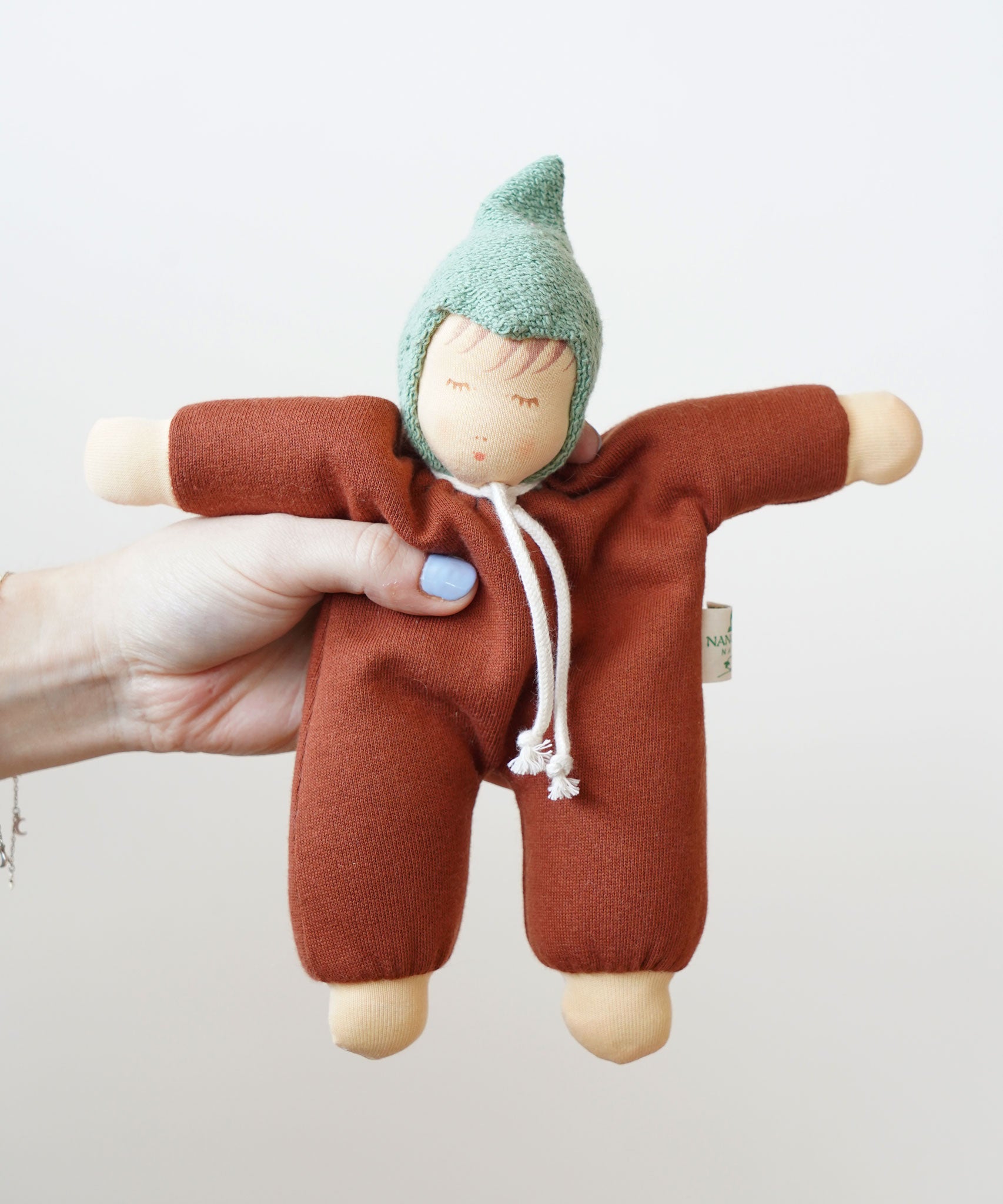 A close up of a Nanchen Walnut Baby Waldorf Doll in an adult's hand.
