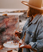 An artist outdoors holding a palette with Natural Earth Paint acrylics painting on a canvas