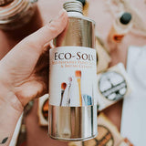 Close up of hand holding the Natural Earth eco-solve paint thinner above some Natural Earth paints