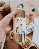 Close up of hand holding the Natural Earth eco-solve paint thinner above some Natural Earth paints