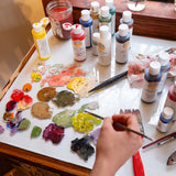 An artist using different Natural Earth Paint acrylic paints mixing different colours on a glass surface.