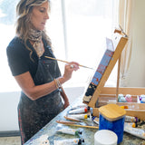 An artist in the studio painting on a canvas with the Natural Earth Pain natural acrylic paints resting on a wooden surface