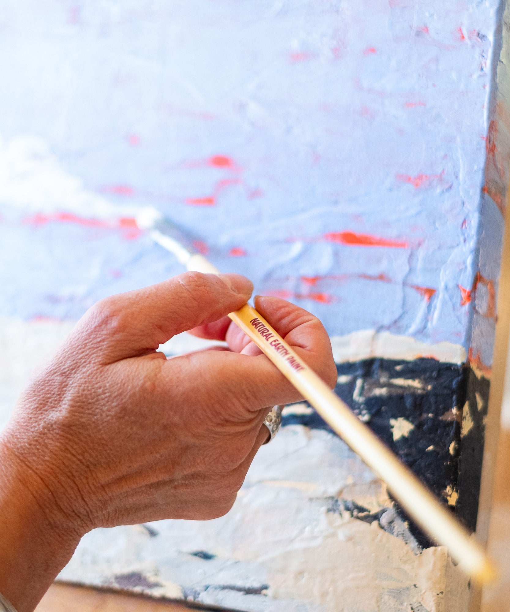 A adult hand holding a Natural Earth paint eco paint brush painting on a painted canvas