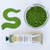 A top down view of the Natural earth paint tube in emerald green next to a bowl of matching paint pigment and a streak showing the consistency.