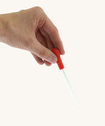 A adult hand holding the Natural Earth Paint glass dropper by the red squeeze handle for size reference