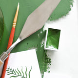 Natural Earth Paint watercolour pan filled with green paint next to a palette knife and brush