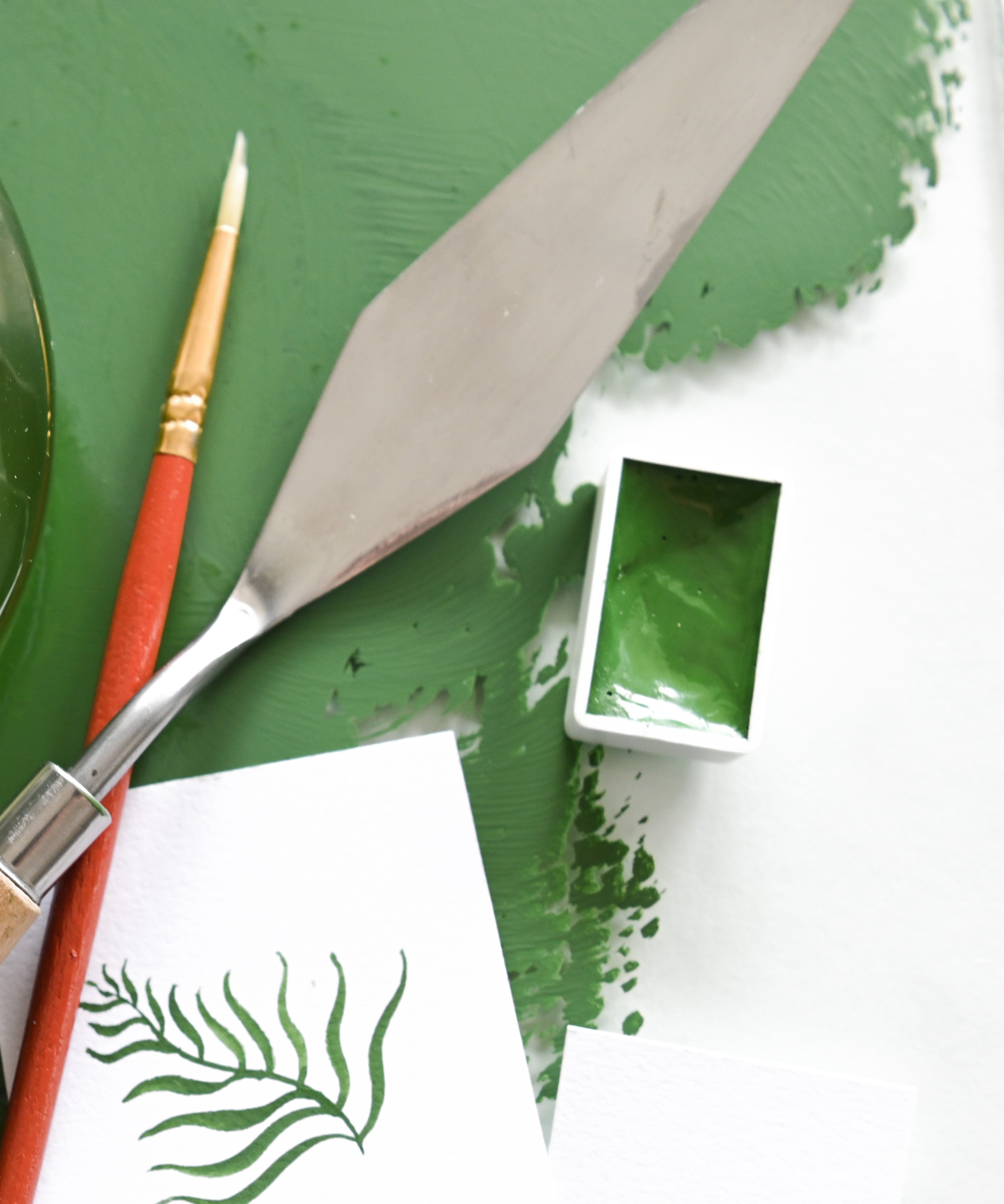 Natural Earth Paint watercolour pan filled with green paint next to a palette knife and brush