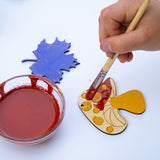 A close up of a child's hands painting a wooden mushroom shaped decoration from the Natural Earth Paint nature craft kit.