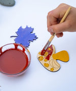 A close up of a child's hands painting a wooden mushroom shaped decoration from the Natural Earth Paint nature craft kit.