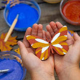 A wooden painted butterfly decoration in a child's hands. The wooden shape has been decorated using natural paints from the Natural Earth Paints Nature Craft Kit.