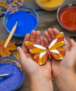 A wooden painted butterfly decoration in a child's hands. The wooden shape has been decorated using natural paints from the Natural Earth Paints Nature Craft Kit.