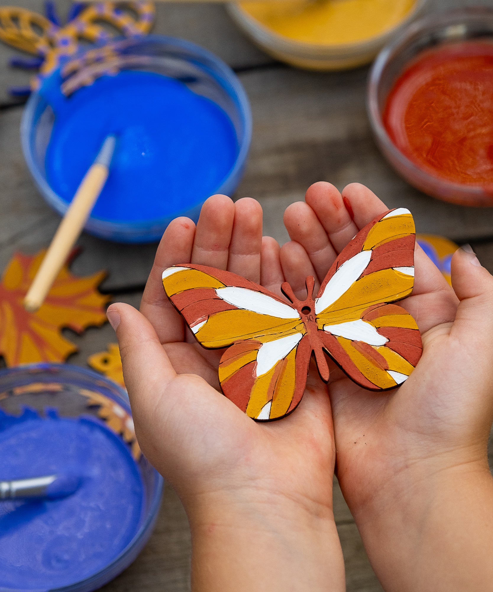 A wooden painted butterfly decoration in a child's hands. The wooden shape has been decorated using natural paints from the Natural Earth Paints Nature Craft Kit.