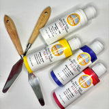 Natural Earth Paint palette knife with wooden handle laid next to white, yellow blue and red acrylic paint