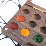 A close up of the Natural Earth Paint small wooden watercolour palette showing different coloured paint in the well