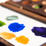 A close up of the Natural Earth Paint small wooden watercolour palette showing different coloured paint ready to be mixed on the white mixing panel