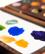 A close up of the Natural Earth Paint small wooden watercolour palette showing different coloured paint ready to be mixed on the white mixing panel