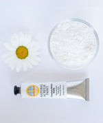 A top down view of the Natural earth paint in titanium white next to the white pigment powder and a white daisy flower