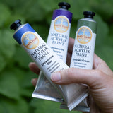 An adult hand holding 3 Natural Earth Paint aluminium tubes for size reference