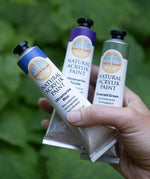 An adult hand holding 3 Natural Earth Paint aluminium tubes for size reference