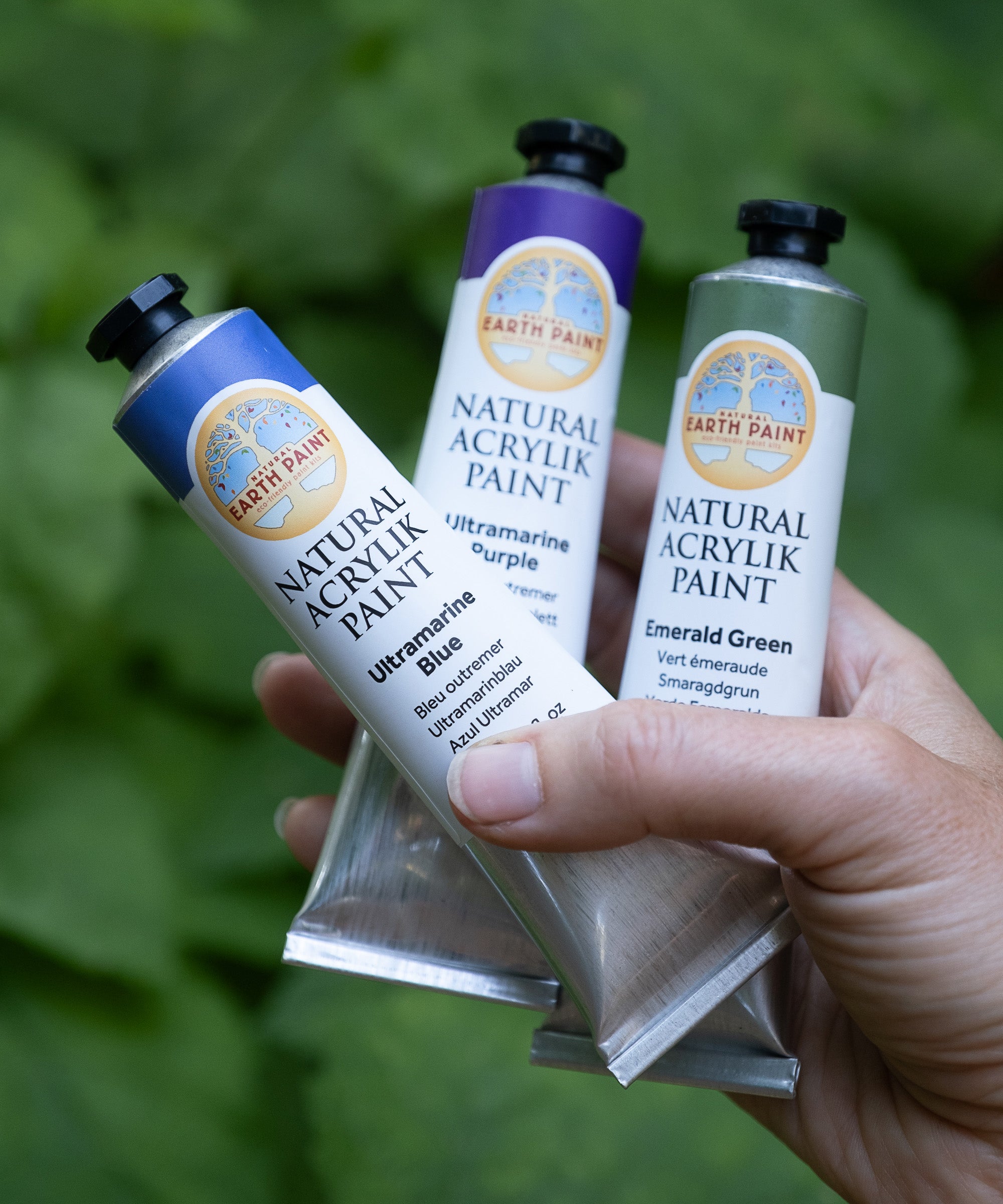 An adult hand holding 3 Natural Earth Paint aluminium tubes for size reference
