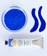A top down view of the Natural earth paint in ultramarine blue next to the blue pigment powder and 2 streaks showing the consistency.