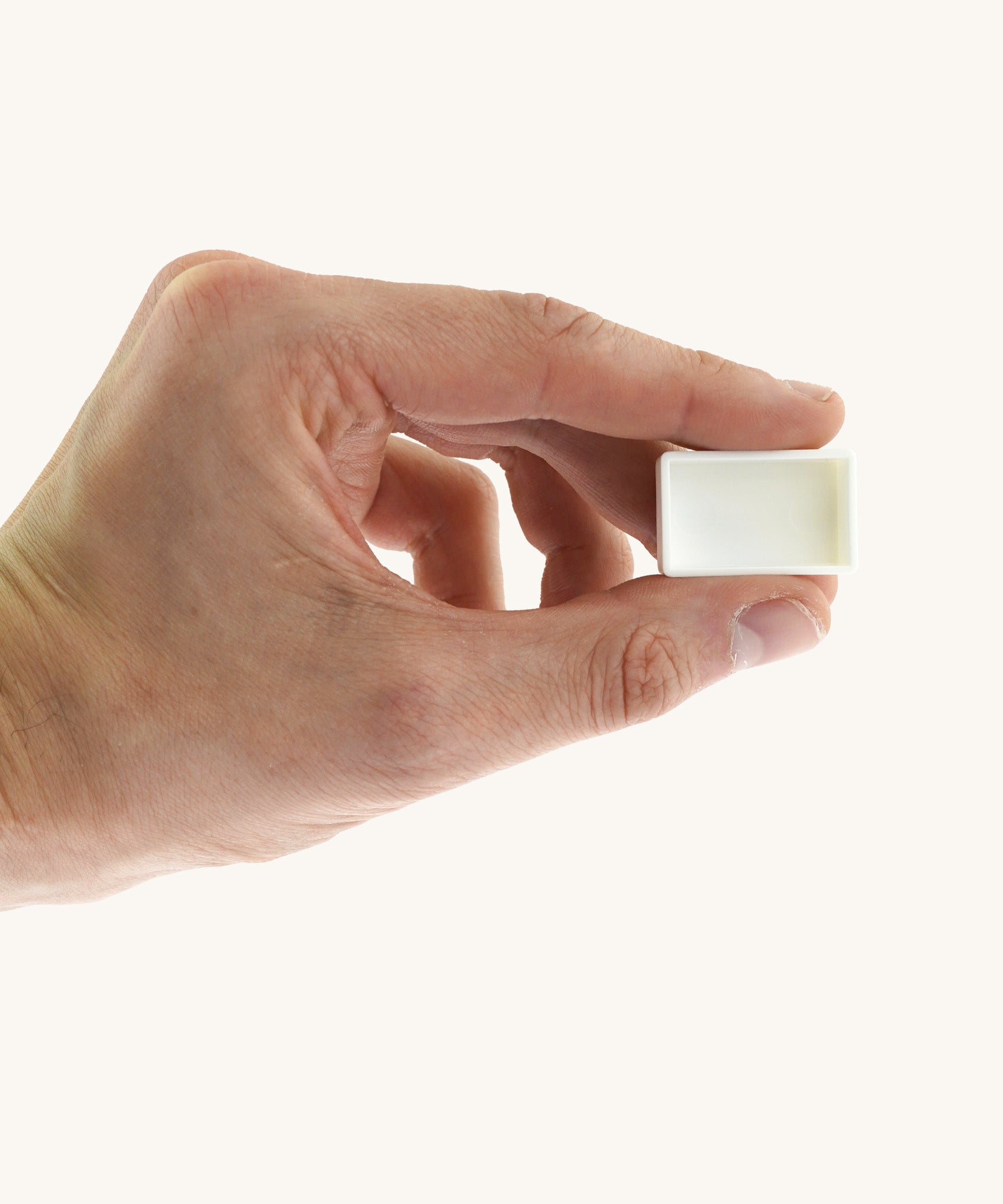 An adult hand holding the white blank watercolour paint pan from Natural Earth Paint  for size reference.