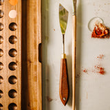 A top down view of the Natural Earth paint watercolour wooden palette with brush holder next to a palette knife and brush