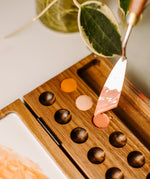 A close up view of the Natural Earth Paint wooden palette showing the palette knife scooping paint from the hole