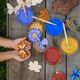 An overhead view of children using the Natural Earth Paint nature craft kit. they can be seen painting and holding their painted wooden decorations