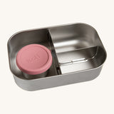 A close up of the One Green Bottle lunchbox showing the 3 different compartments inside separated by a divided. Comes with a little snack pot with a pale pink silicone lid.