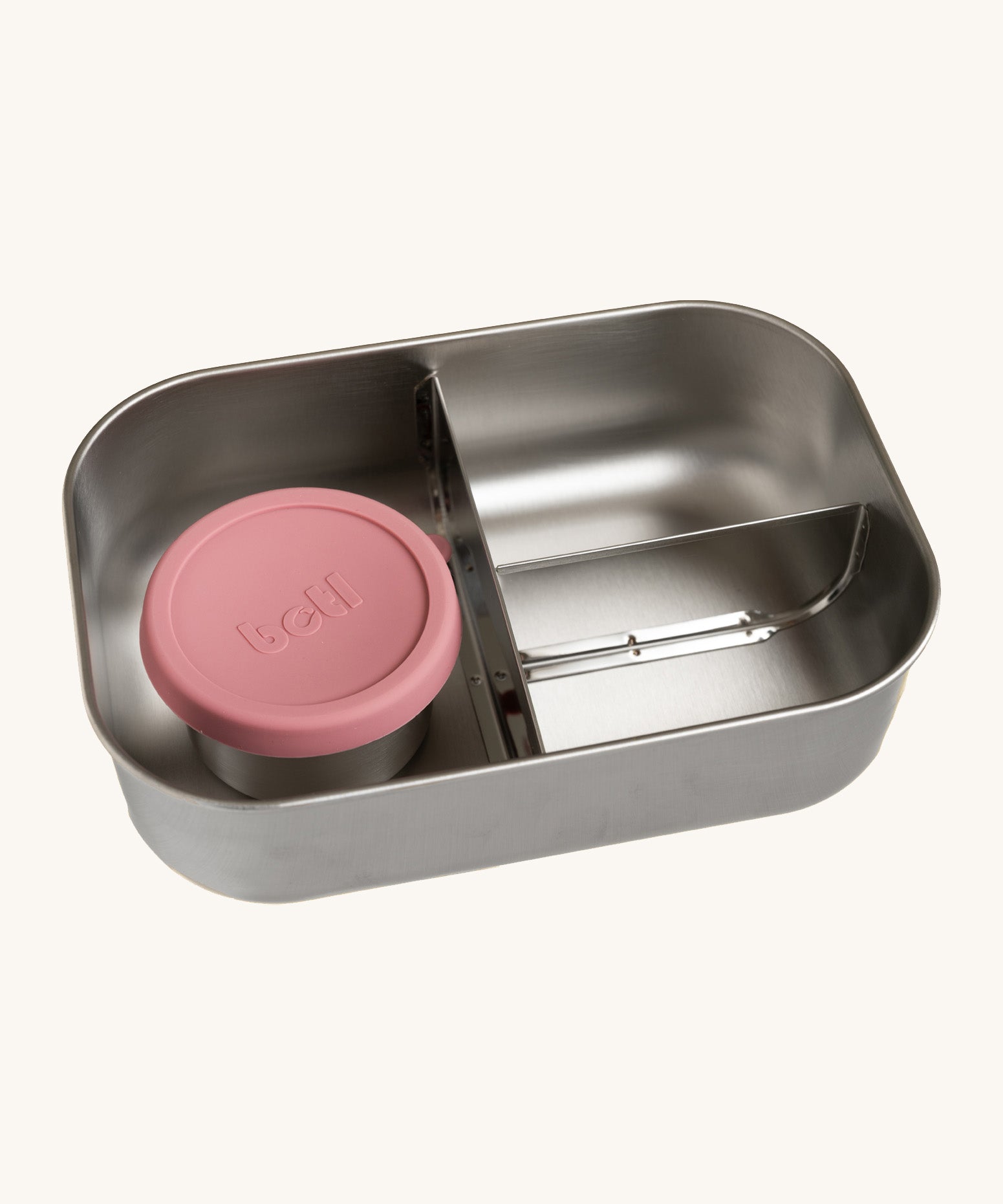 A close up of the One Green Bottle lunchbox showing the 3 different compartments inside separated by a divided. Comes with a little snack pot with a pale pink silicone lid.