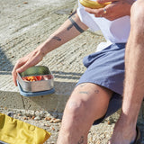 A close up of a man holding a One Green Bottle lunchbox in soldier showing the different compartments inside.